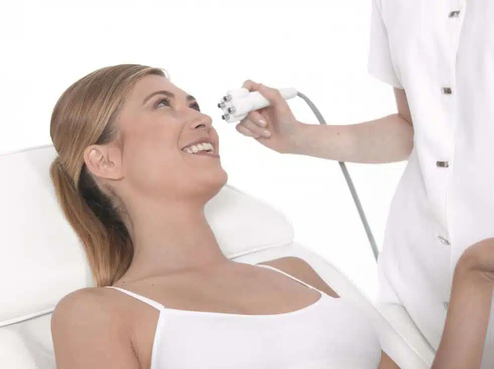 A smiling woman receiving a Venus Legacy skin tightening treatment on her face from a practitioner in a clean clinical setting