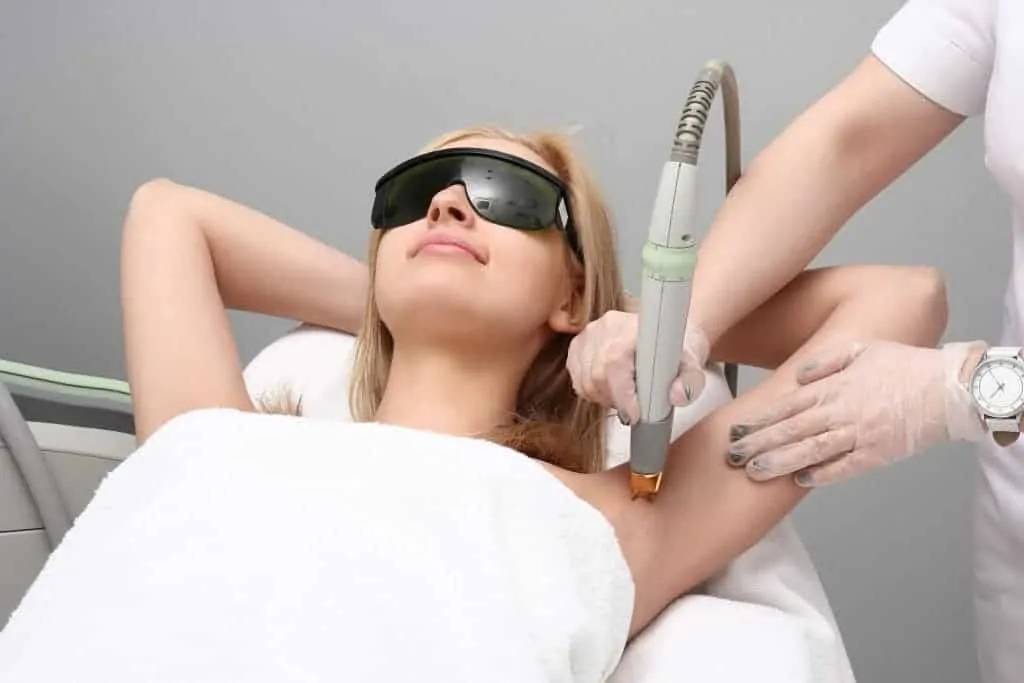 A woman receiving a laser hair removal treatment under her arm, wearing protective eyewear in a clean clinical setting